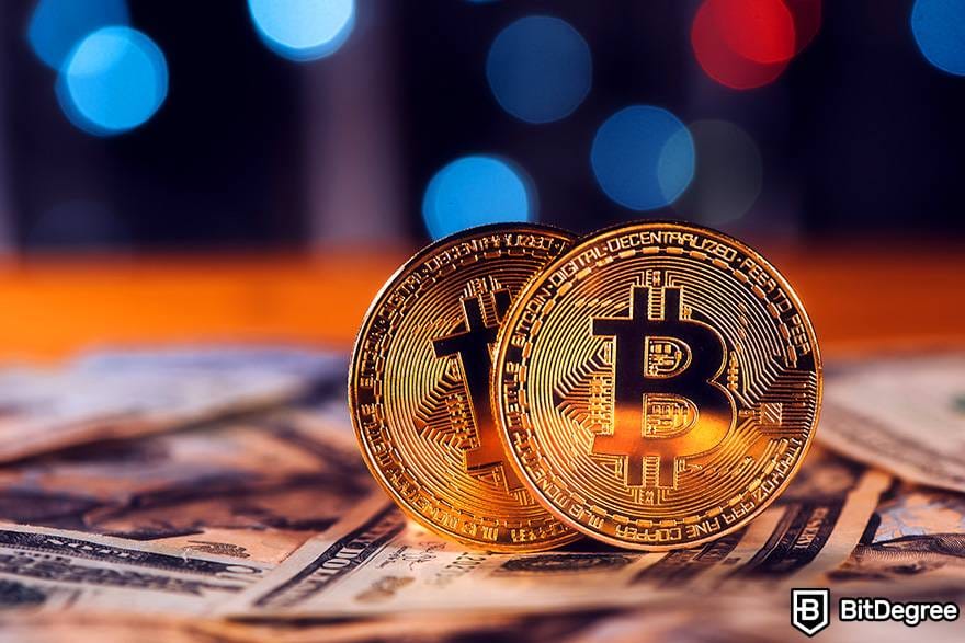 Kriptoya nasıl yatırım yapılır: İki fiziksel bitcoin madeni para, bir yığın dolar banknotunun üzerine yerleştirilir.