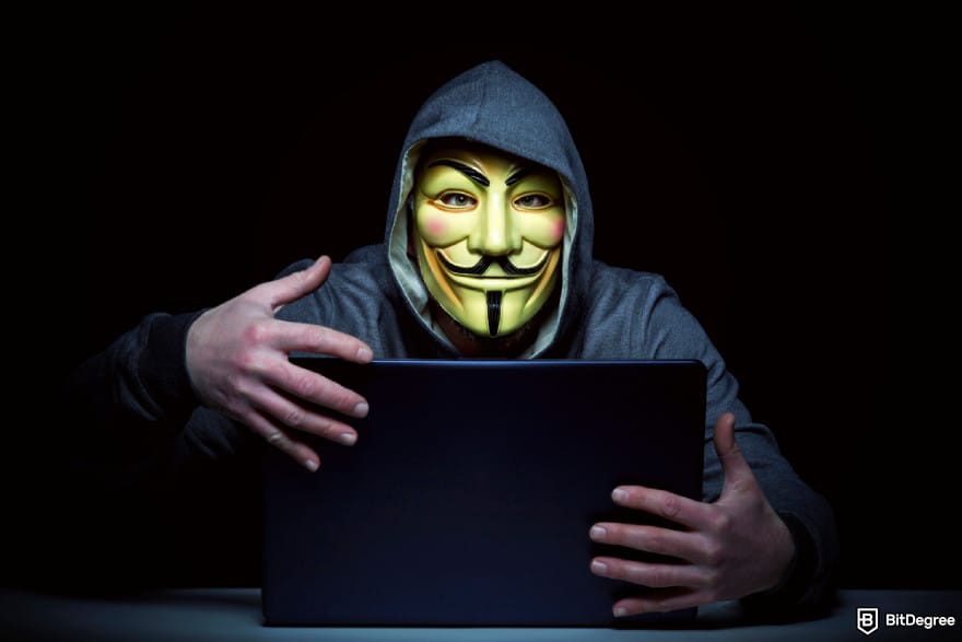 Что такое Pi Network: человек в маске и худи, сидящий в темном помещении с ноутбуком.